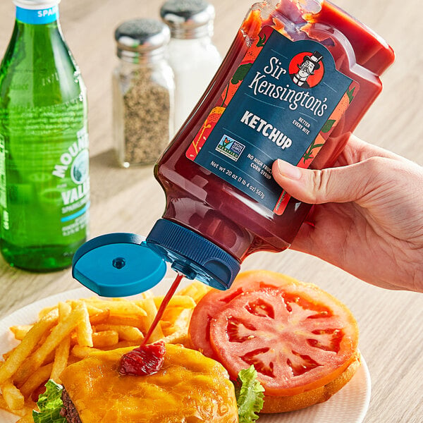 A hand holding a Sir Kensington's classic ketchup squeeze bottle over a plate of food.