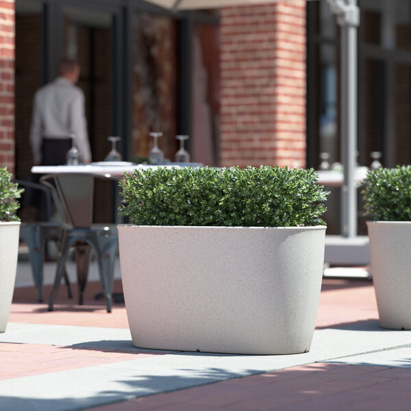 Three Lancaster Table & Seating Marie gray planters on an outdoor patio table filled with plants in white pots.