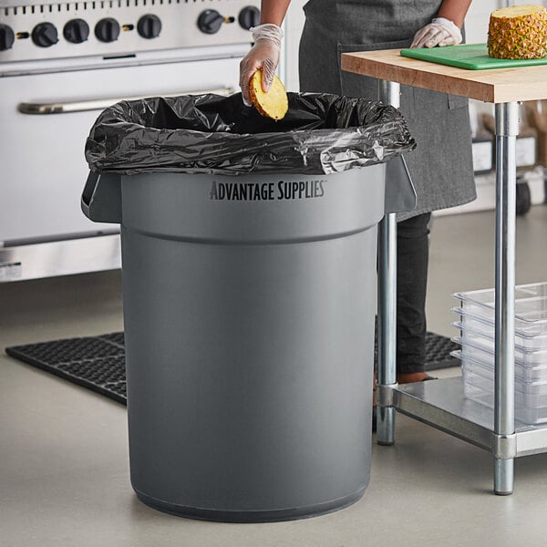 A woman putting a sponge into a grey Advantage Supplies commercial trash can with a black bag.