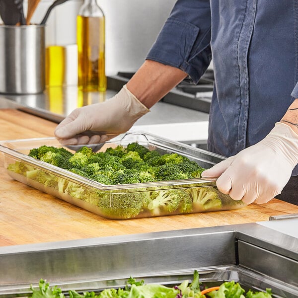 A person preparing broccoli in a Vollrath clear polycarbonate food pan.