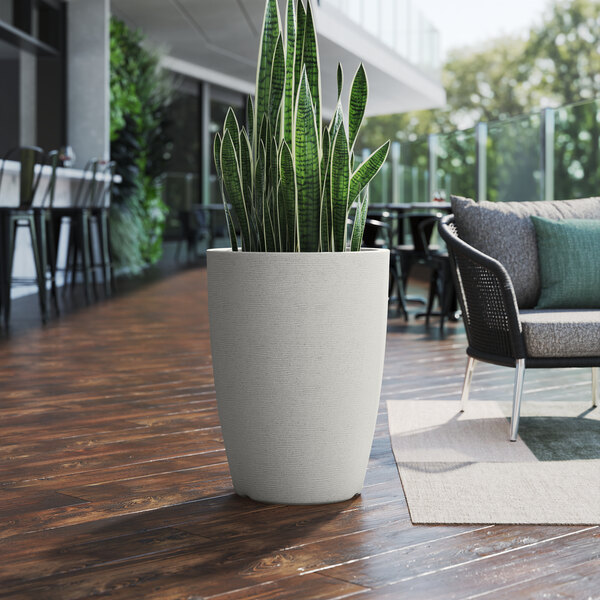 A Lancaster Table & Seating gray planter with a potted plant on a wood floor.