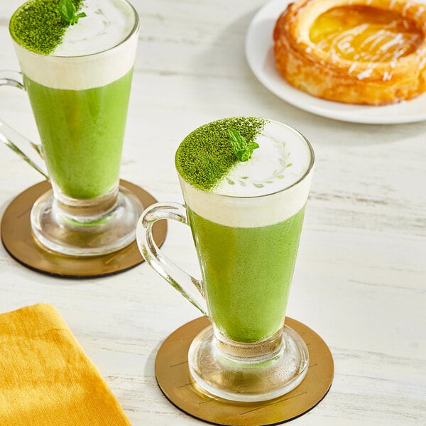 Two glasses of Tenzo Organic Sweetened Matcha Latte on a table with a yellow cloth.