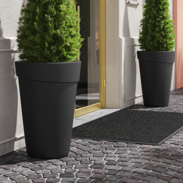 Two Lancaster Table & Seating black planters with plants in them.