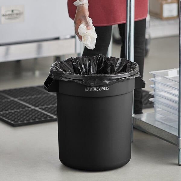 A man in a black jacket putting a white tissue in a black Advantage Supplies commercial trash can.