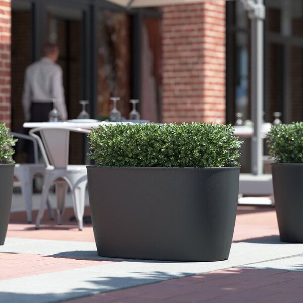 A group of Lancaster Table & Seating Marie black planters on an outdoor patio table with plants inside.