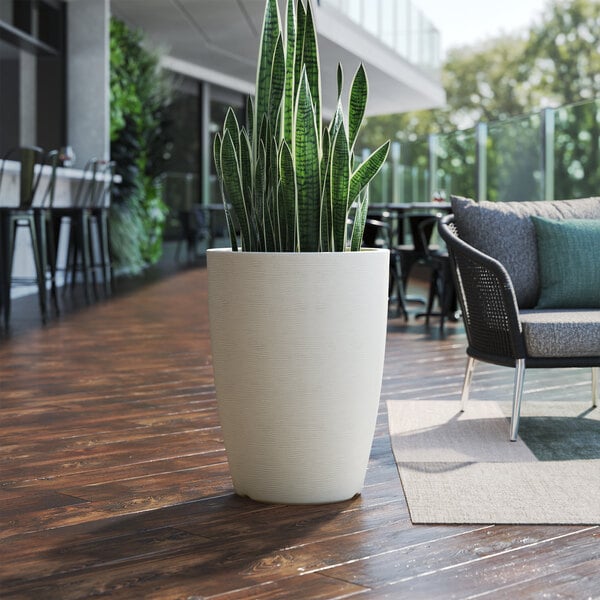 A white Lancaster Table & Seating planter with a potted plant on a wooden deck.