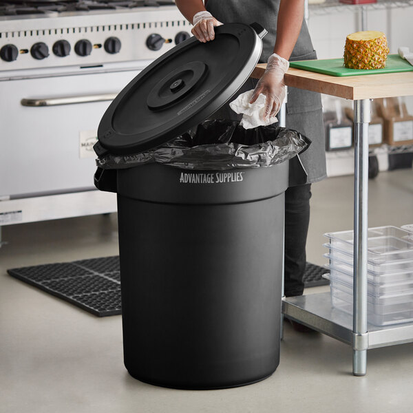 A woman putting a garbage bag in a black round commercial trash can.