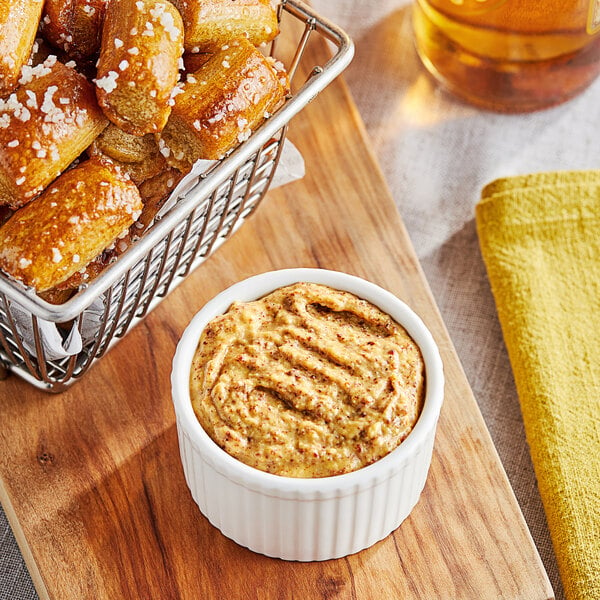 A bowl of Sir Kensington's spicy brown mustard on a table with food.