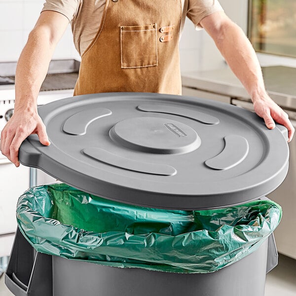 A man wearing an apron putting a gray lid on a 55-gallon round trash can.