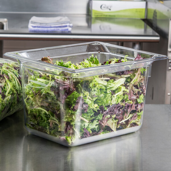 A clear plastic Vollrath 8028410 food pan filled with lettuce sitting on a counter.