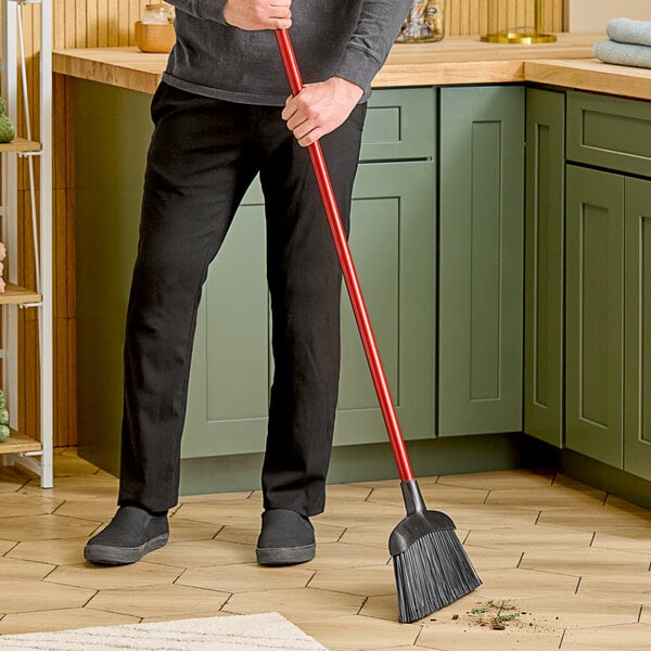 A person using a Libman commercial angle broom to sweep the floor in a professional kitchen.