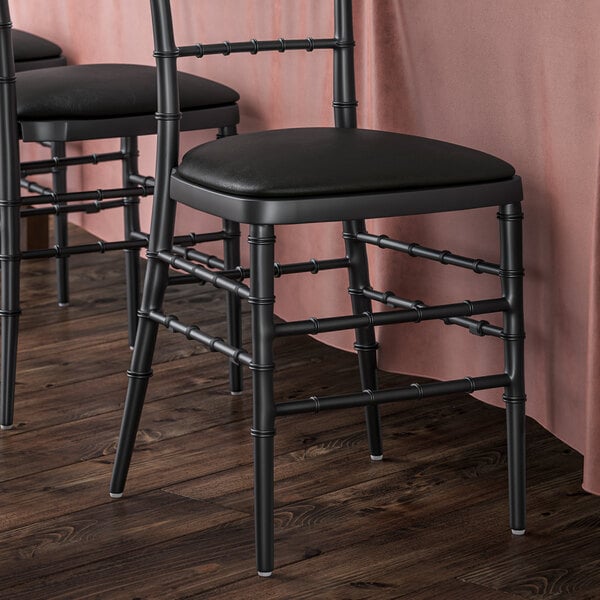 Three black Lancaster Table & Seating Chiavari chairs with black vinyl cushions.