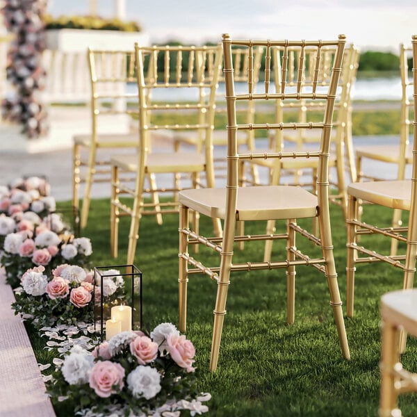 A row of gold Lancaster Table & Seating Chiavari chairs with flowers on the grass.