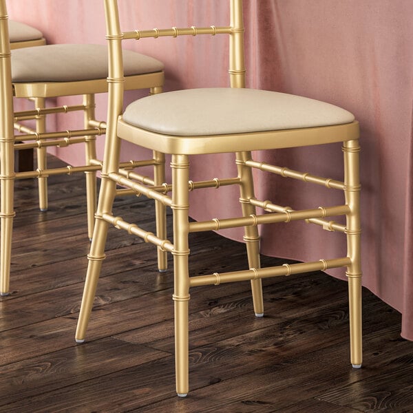 A pair of gold Lancaster Table & Seating Chiavari chairs with ivory cushions.