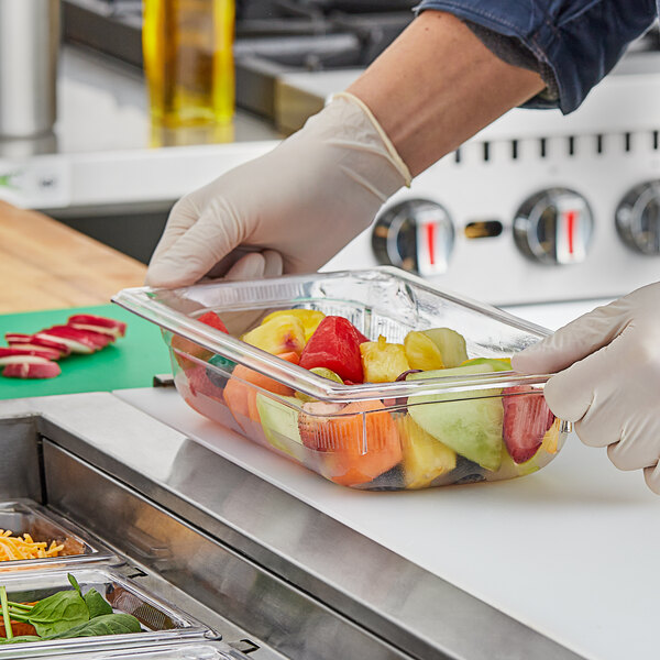 A person in gloves preparing fruit in a Vollrath clear polycarbonate food pan on a counter.