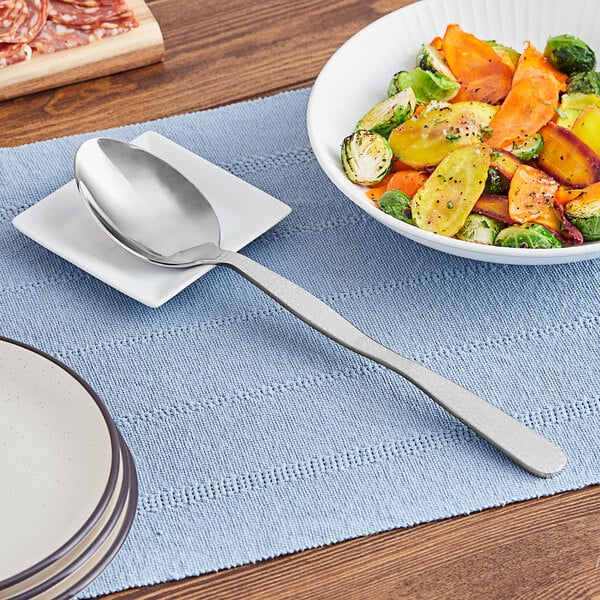 A plate with a spoon on it next to a bowl of vegetables.