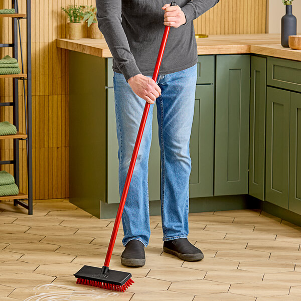 A man using a Libman red floor scrub to clean the floor.
