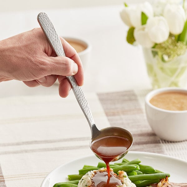 A person using an American Metalcraft stainless steel ladle to pour sauce over a plate of food.