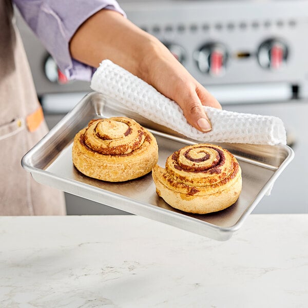 A person holding a Baker's Lane aluminum sheet pan with cinnamon rolls.