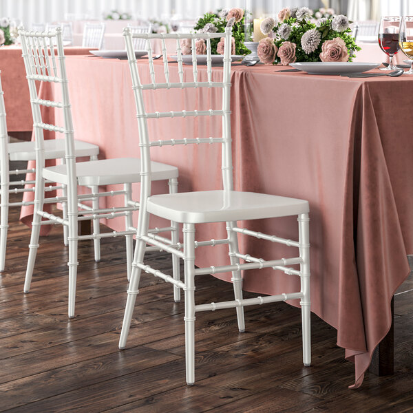 A table with a pink tablecloth and Lancaster Table & Seating white chiavari chairs.
