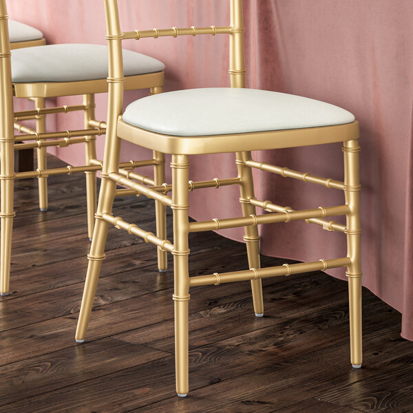 A pair of gold chiavari chairs with white cushions.