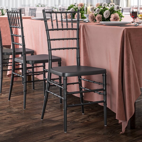 A table with a pink tablecloth and black Lancaster Table & Seating Chiavari chairs.
