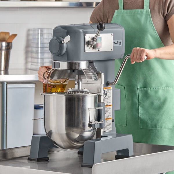 A commercial planetary stand mixer with a stainless steel mixing bowl and safety guard, being used in a kitchen setting.