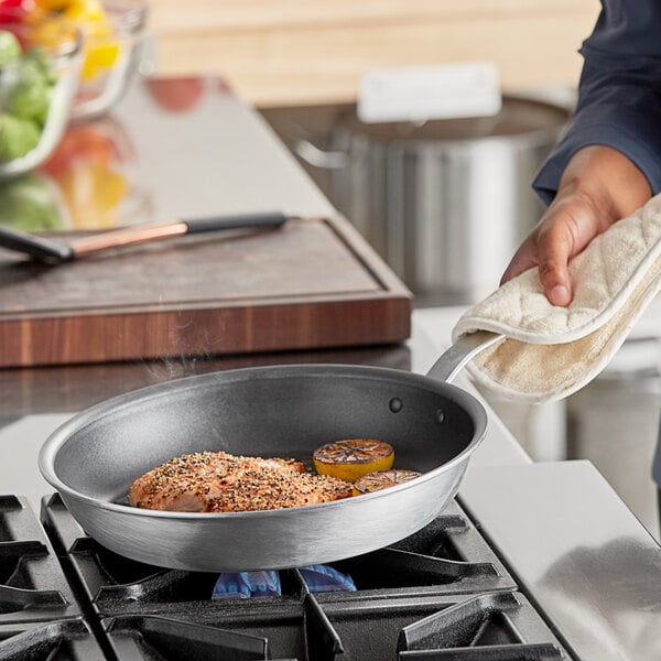 A person cooking food in a Vigor aluminum fry pan on a stove.