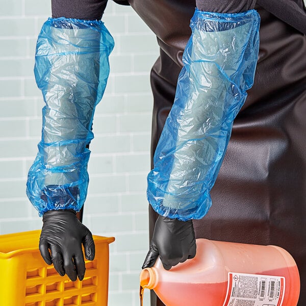 A person wearing black gloves and Lavex blue plastic sleeves pouring liquid into a container.