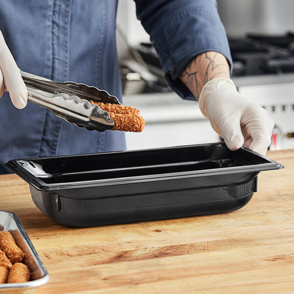 A person in gloves using a Vollrath black polycarbonate food pan to serve food.