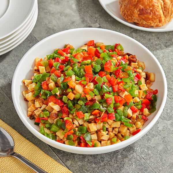 A bowl of Savor Imports IQF red and green diced peppers on a table with a spoon.