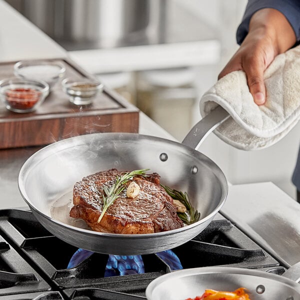 A piece of steak with garlic and rosemary cooking in a Vigor A3000 series aluminum fry pan.