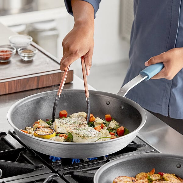 A person cooking vegetables in a Vigor A3000 Series aluminum fry pan.