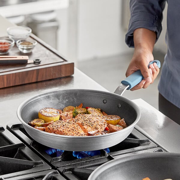 A person using a Vigor aluminum fry pan to cook food on a stove.