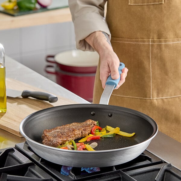 A person cooking meat and vegetables in a Vigor aluminum frying pan with a silicone grip.