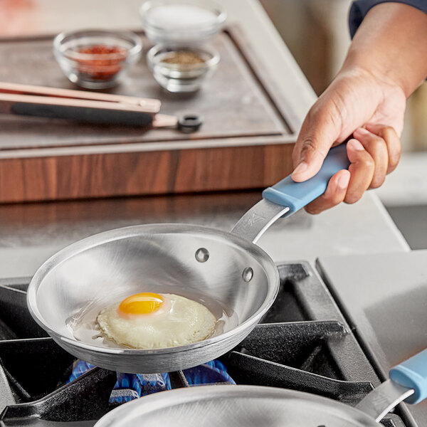 A person cooking a fried egg in a Vigor A3000 Series aluminum fry pan.