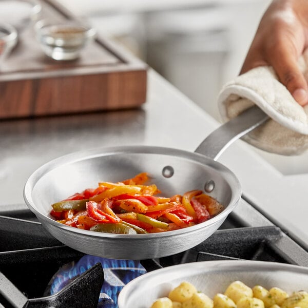 A person using a Vigor aluminum fry pan to cook food on a stove.