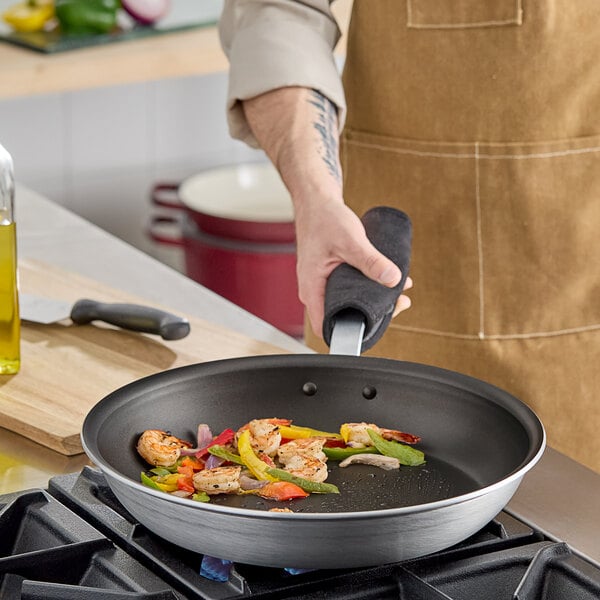 A person cooking shrimp and vegetables in a Vigor A3000 Series aluminum frying pan with a plated handle.