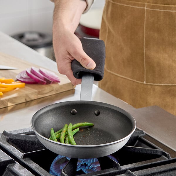 A person cooking green beans and sliced onions in a Vigor A3000 Series aluminum frying pan with a plated handle.