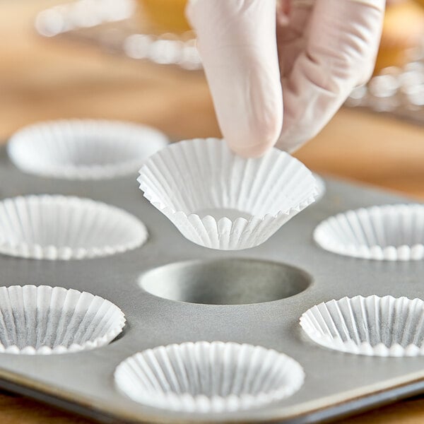 A hand holding a white fluted mini baking cup.