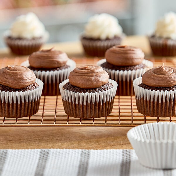 A group of chocolate cupcakes in white fluted paper baking cups on a cooling rack.