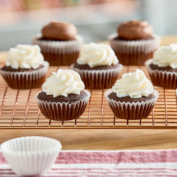 A group of chocolate cupcakes with white frosting in 1 1/2" x 1" white fluted mini baking cups on a cooling rack.