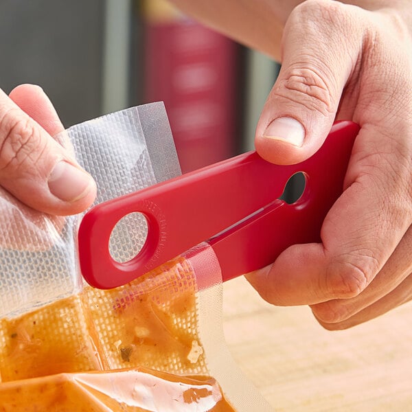 A person using a red Tangibles Super Snippit to cut open a bag of food.