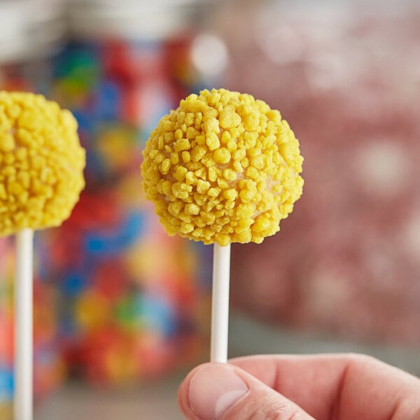 A close up of a hand holding yellow Yum Crumbs Lemon Pound Cake pops.