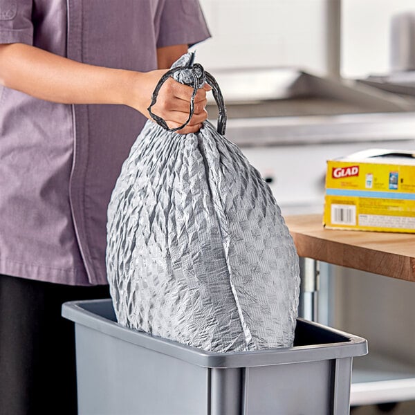 A woman holding a Glad ForceFlex white trash bag with a drawstring.