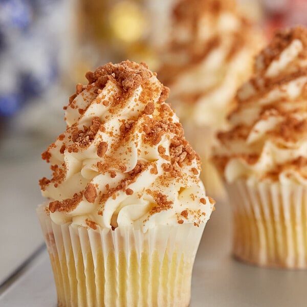 A cupcake with white frosting and Yum Crumbs brown crumbs on top.