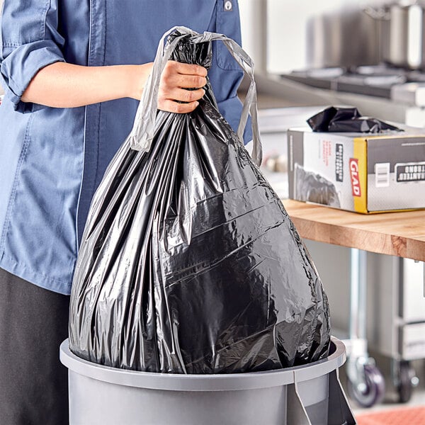 A woman holding a black Glad drawstring trash bag.