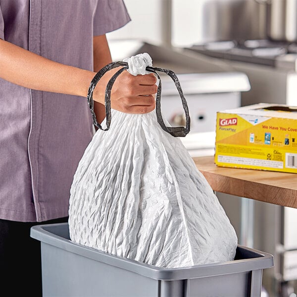 A person holding a white plastic bag of trash in a trash can.