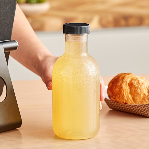 A hand holding a 16 oz. PET clear sauce bottle filled with yellow liquid.