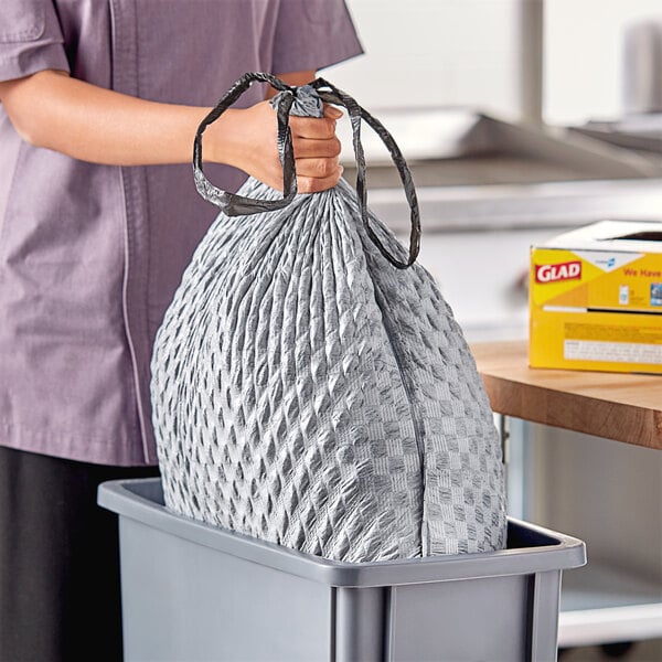 A woman's hand holding a Glad CloroxPro grey trash bag over a trash can.